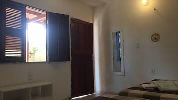 A bedroom with a bed, a wardrobe, a window with blinds, and a wall-mounted light fixture.