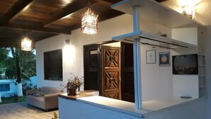 A modern outdoor kitchen area with a white countertop, a wooden door, and a hanging light fixture. - Pousada Brisa Del Mar (Amontada)