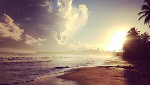 A beach with waves, palm trees, and a sunset. - Pousada Brisa Del Mar (Amontada)