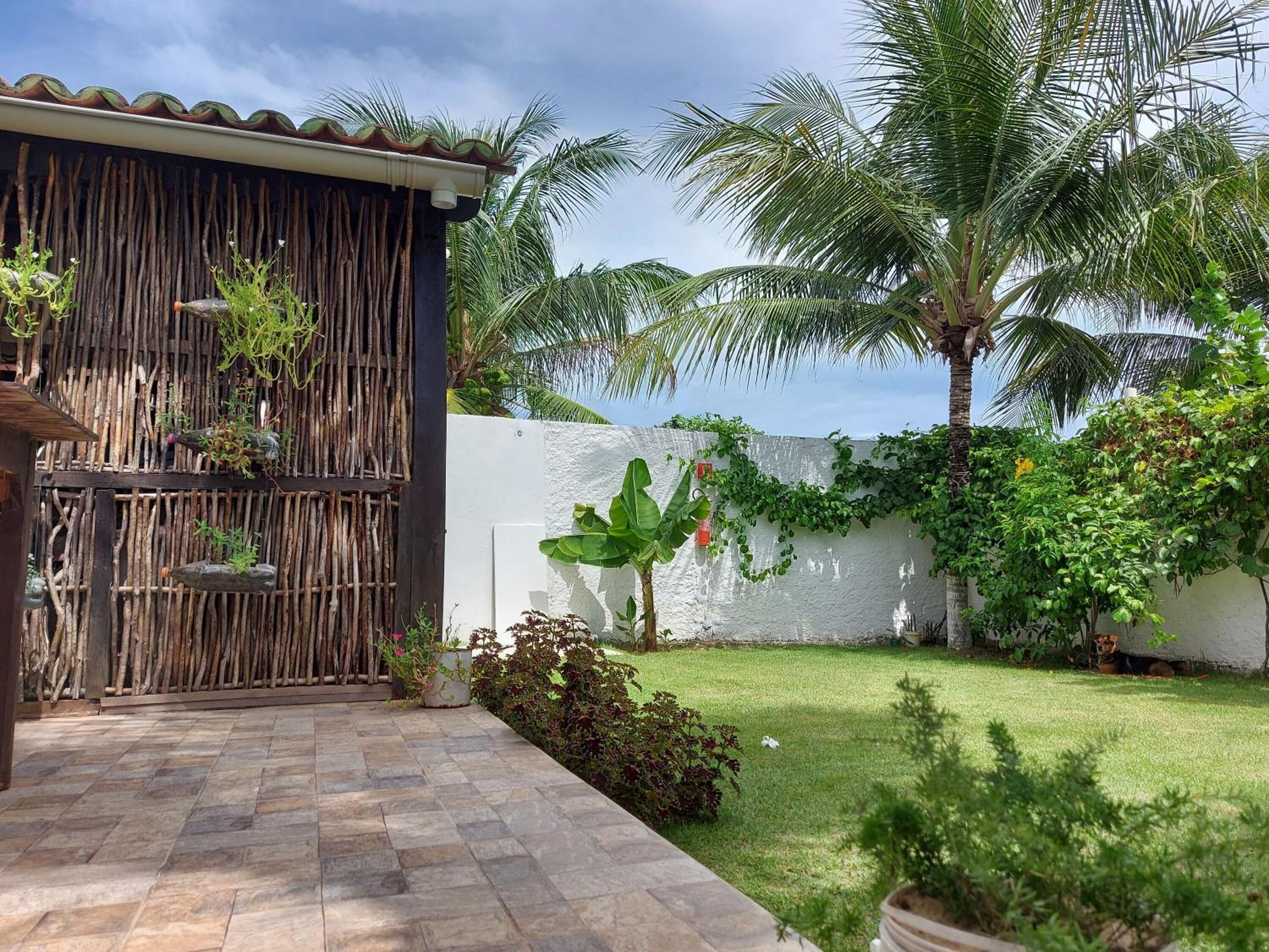 A patio with stone tiles, a bamboo fence, and a white wall with greenery.