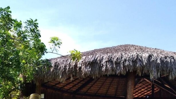 A table with a bottle, a glass, and a bucket, set outdoors under a thatched roof. - Pousada Brisa Del Mar (Amontada)