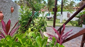 A tropical garden with a thatched-roof gazebo, potted plants, and a stone wall. - Pousada Brisa Del Mar (Amontada)