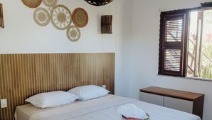 A neatly arranged bedroom with a bed, bedside tables, a hanging light fixture, and a window with blinds. - Pousada Brisa Del Mar (Amontada)