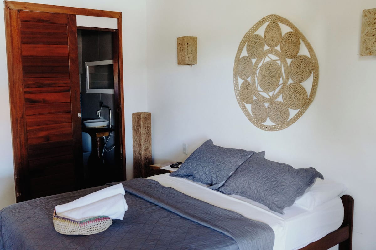 Un dormitorio con una cama, una puerta de madera, un adorno circular fijado a la pared y una pequeña mesa con una silla.