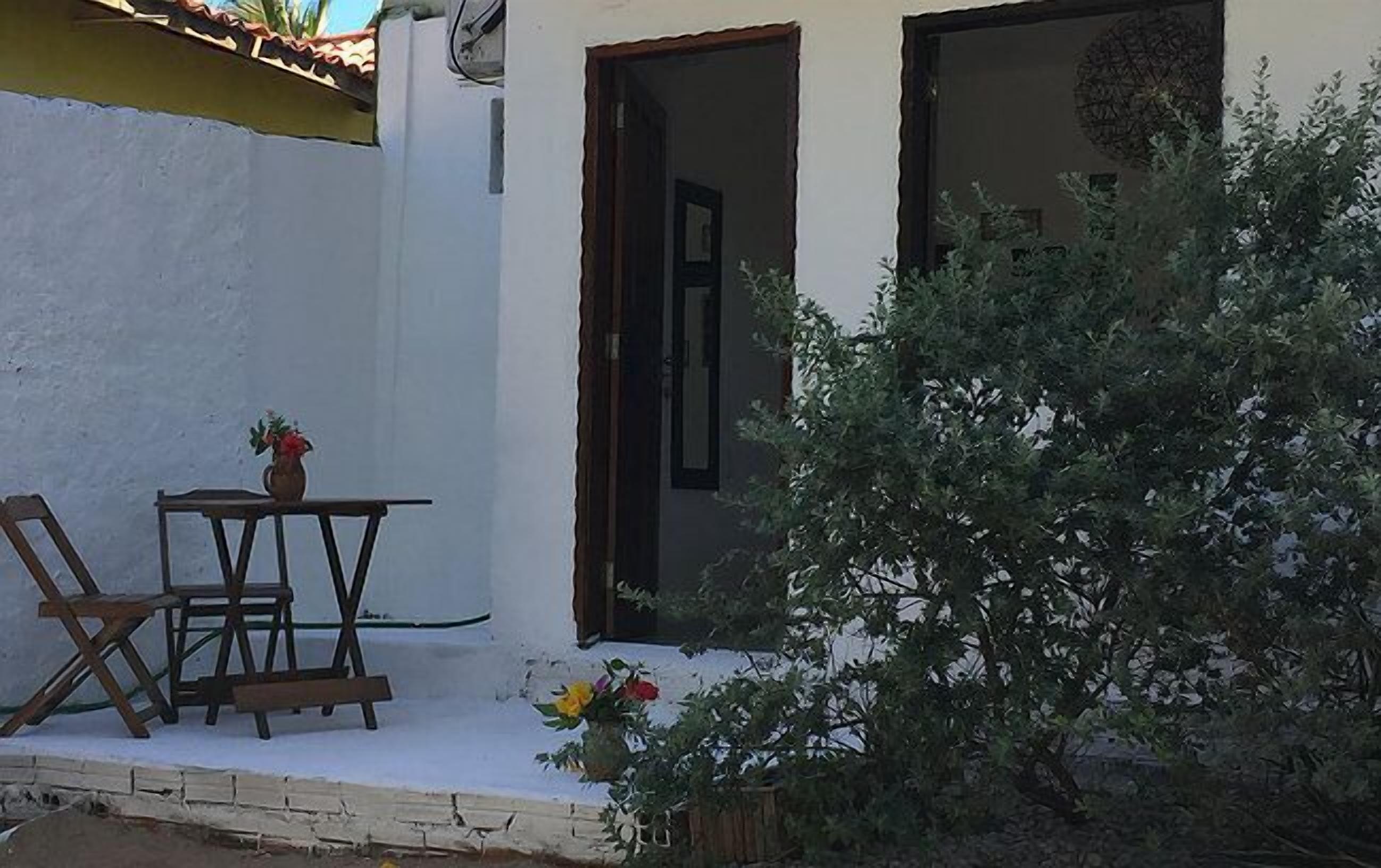 A small outdoor seating area with a table and chairs, a potted plant, and a doorway leading to a building.