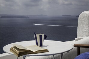 A round table with a book and a striped cup, overlooking a body of water with a boat in the distance. - Lava Caves (Santorini)