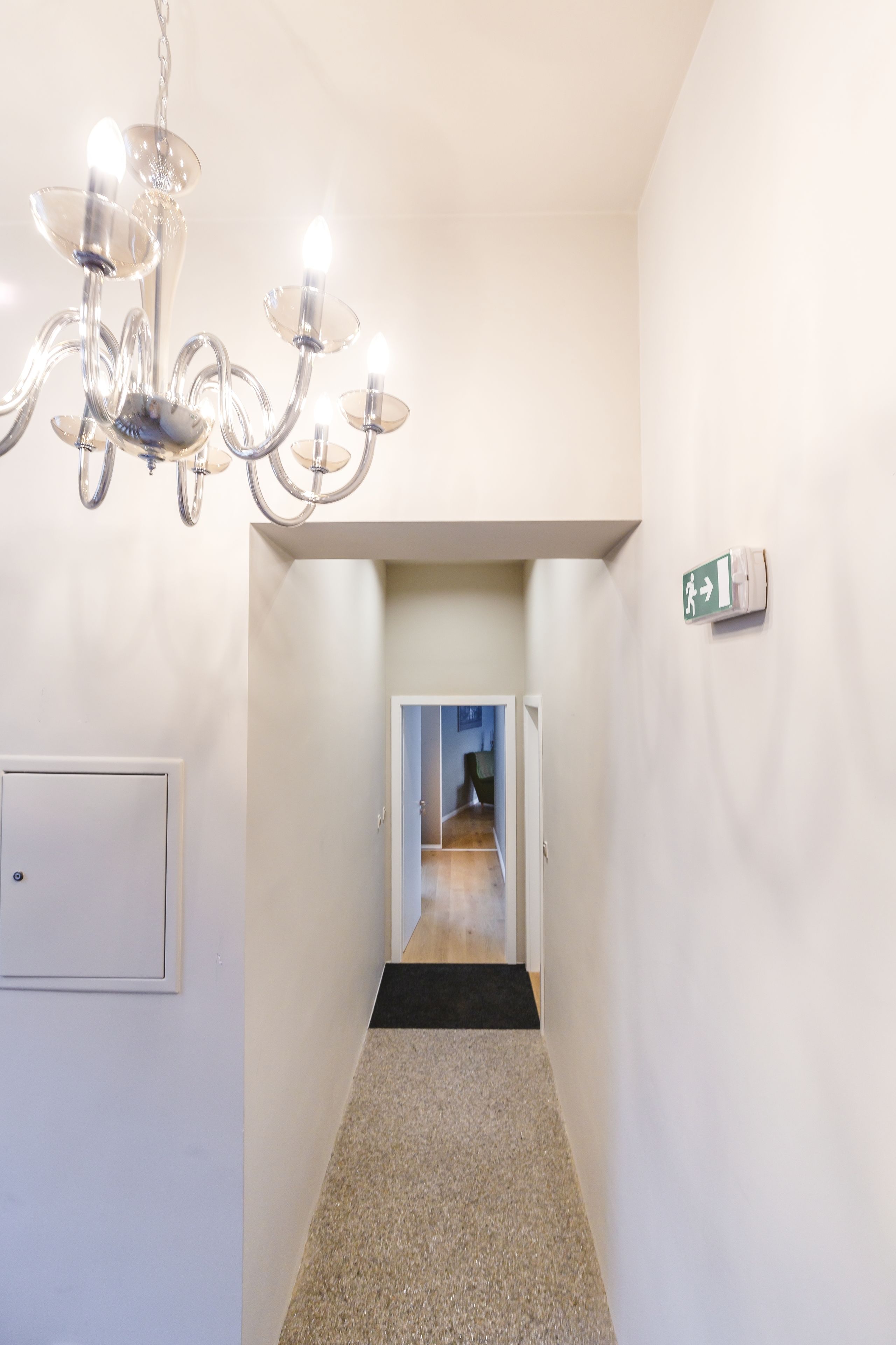 Un couloir avec un lustre, une porte et un panneau indiquant la sortie de secours.