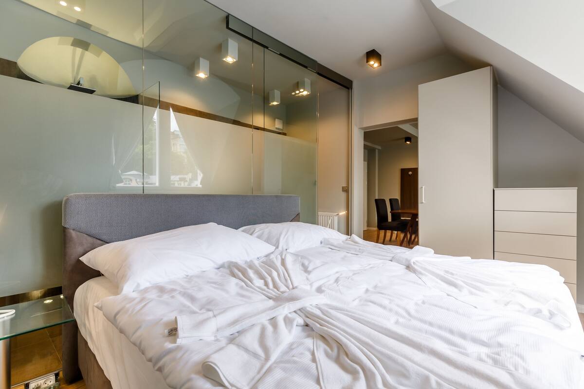 Ein modernes Schlafzimmer mit einem großen Bett, einer Trennwand aus Glas und Blick auf einen Essbereich.