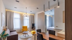 Quarto de hotel moderno com sofá, mesa de jantar, cadeiras, televisão e cama.