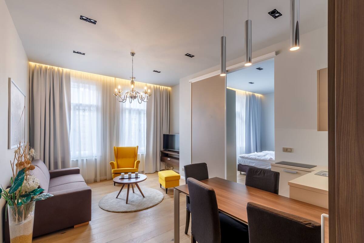 Ein modernes Hotelzimmer mit einer Couch, einem Esstisch, Stühlen, einem Fernseher und einem Bett.