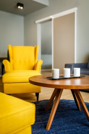 A modern living room with a yellow armchair, a round wooden coffee table with three candles, and a blue carpet.