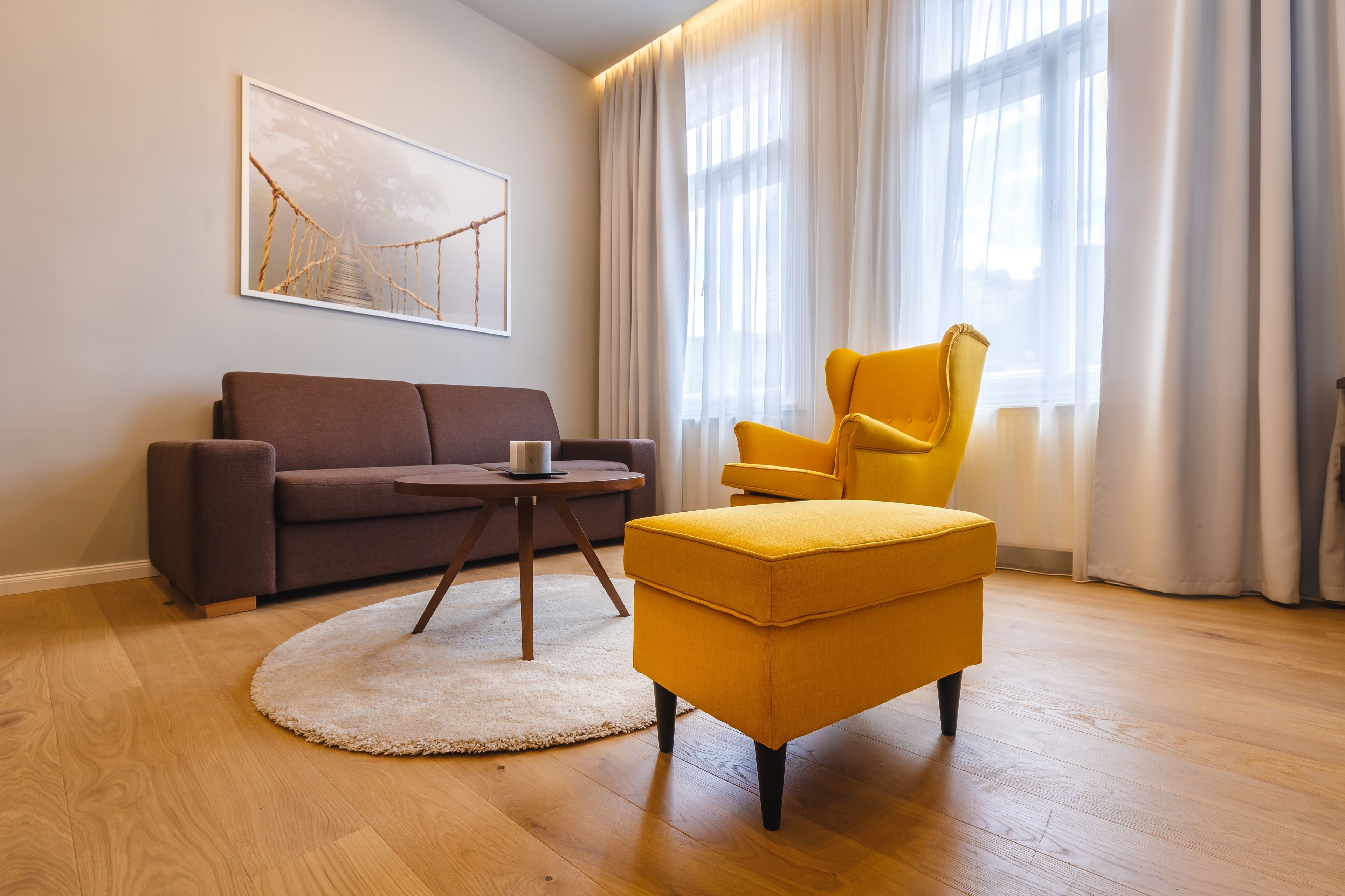 A living room with a brown sofa, a yellow armchair, a small round table, and a white rug.