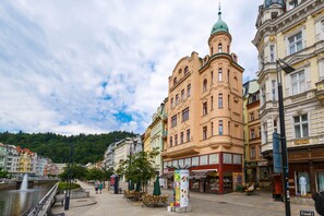 A historic building with a green dome, adjacent shops, and a fountain in a public square. - Apartments Bohemia Rhapsody (Karlovy Vary)
