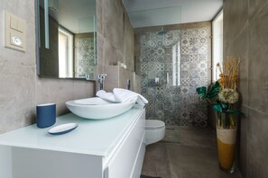 A modern bathroom with a large mirror, a white sink, a blue cup, and a vase with dried flowers. - Apartments Bohemia Rhapsody (Karlovy Vary)