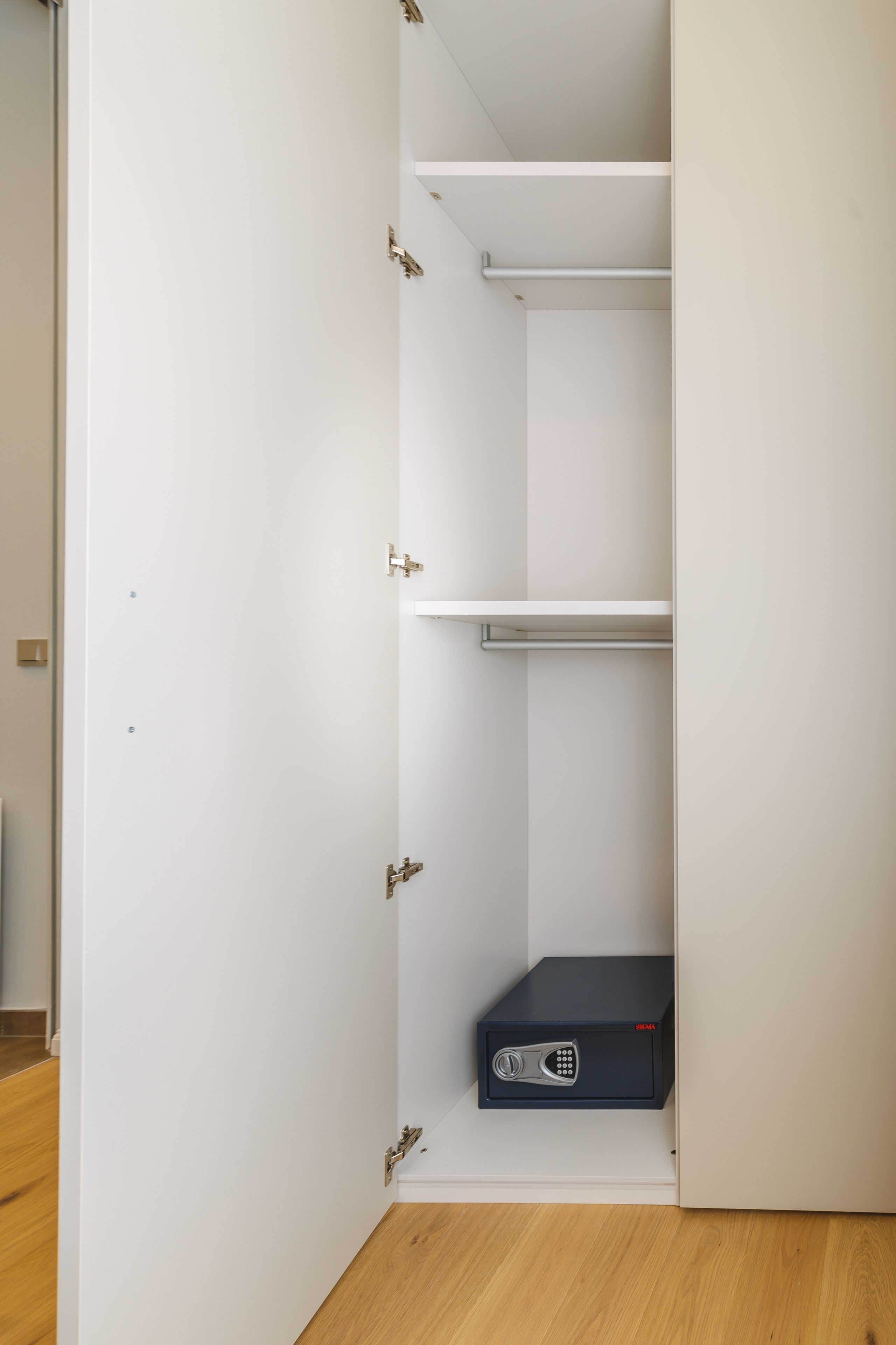 A white wardrobe with a black safe, a wooden floor, and a white wall.