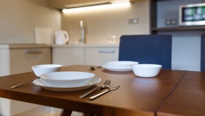 Uma mesa de jantar com pratos brancos, talheres e tigelas, em uma cozinha moderna com micro-ondas e armários ao fundo.