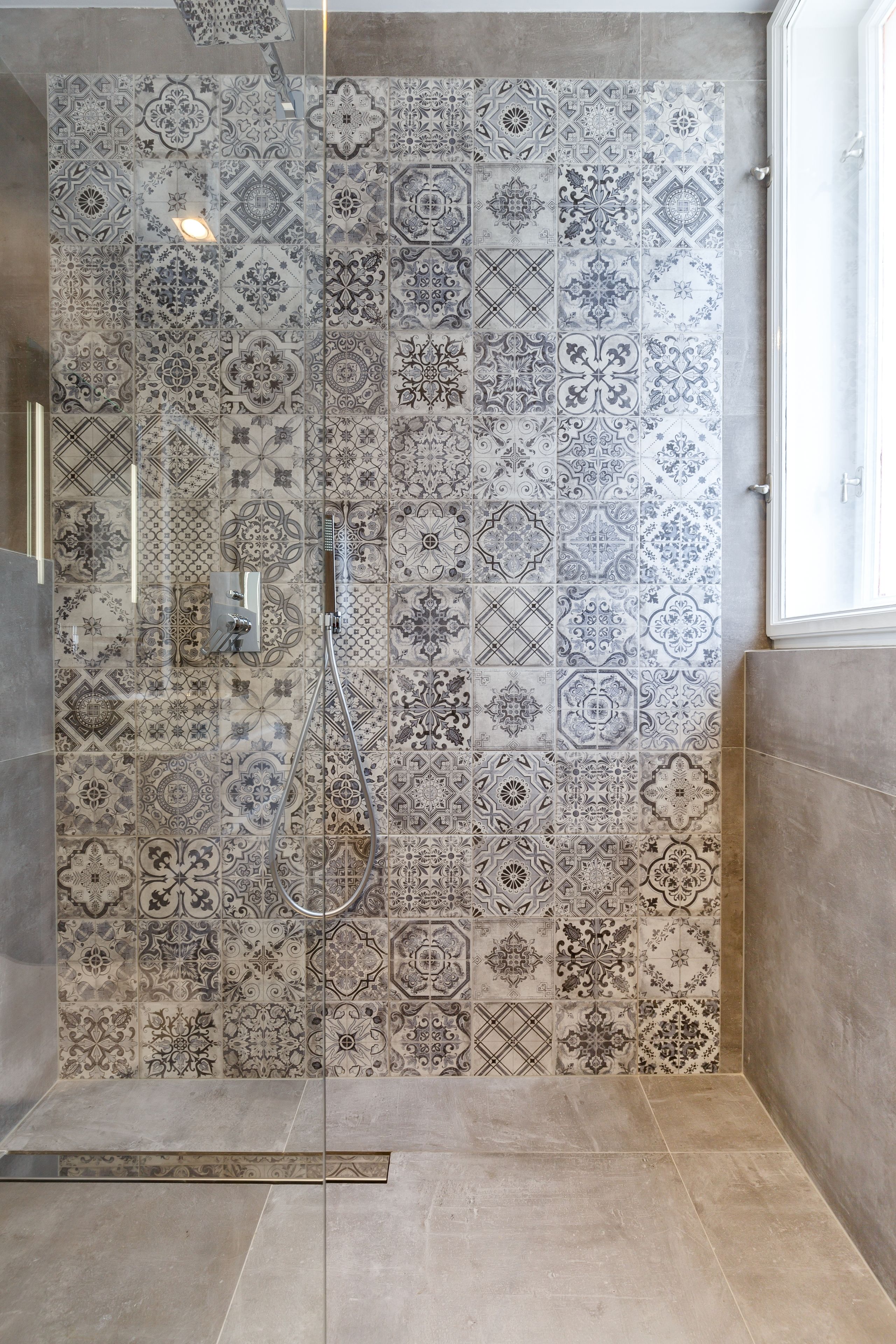 A shower with a complex tile pattern and a handheld showerhead.