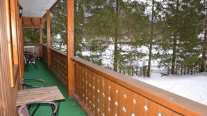 A wooden balcony with a green floor, wooden railings, and a view of a snowy forest. - Apartments Lake Bohinj (Bohinj)