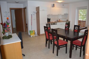 A modern kitchen with white cabinets, a dining table with six chairs, and a small island with a vase of flowers. - Apartments Lake Bohinj (Bohinj)