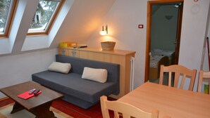 A compact living space with a sofa, a small table, a wooden dining table, and a kitchen area with a basket on the counter. - Apartments Lake Bohinj (Bohinj)
