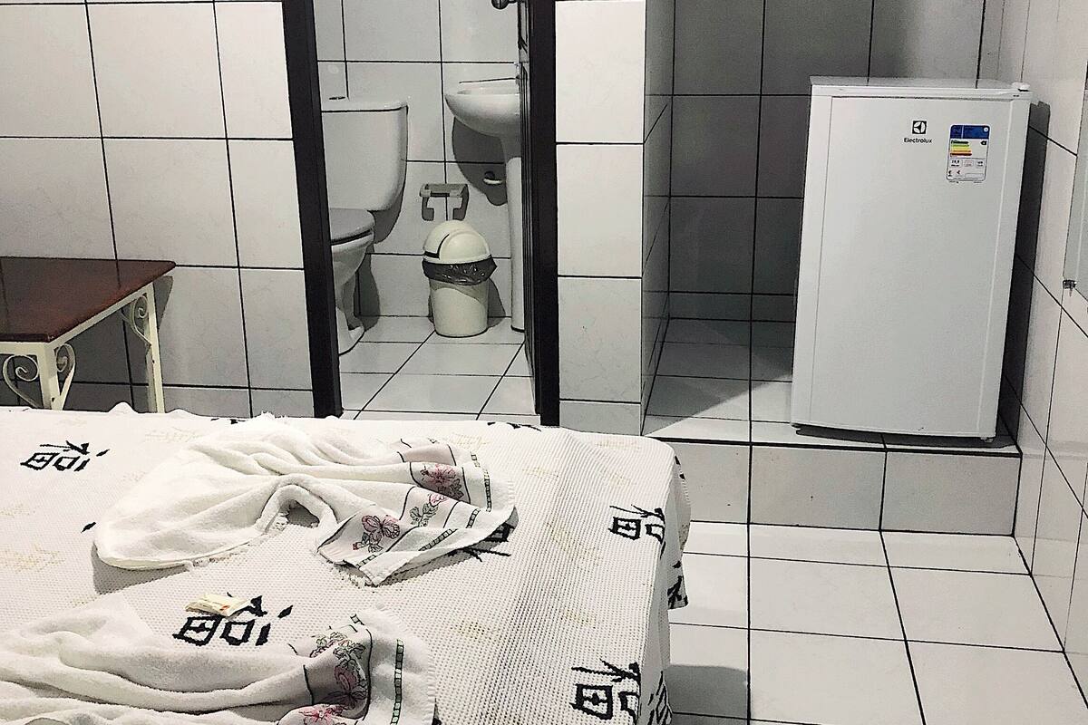 Une petite salle de bain carrelée, équipée de toilettes, d’un bidet et d’un réfrigérateur blanc.