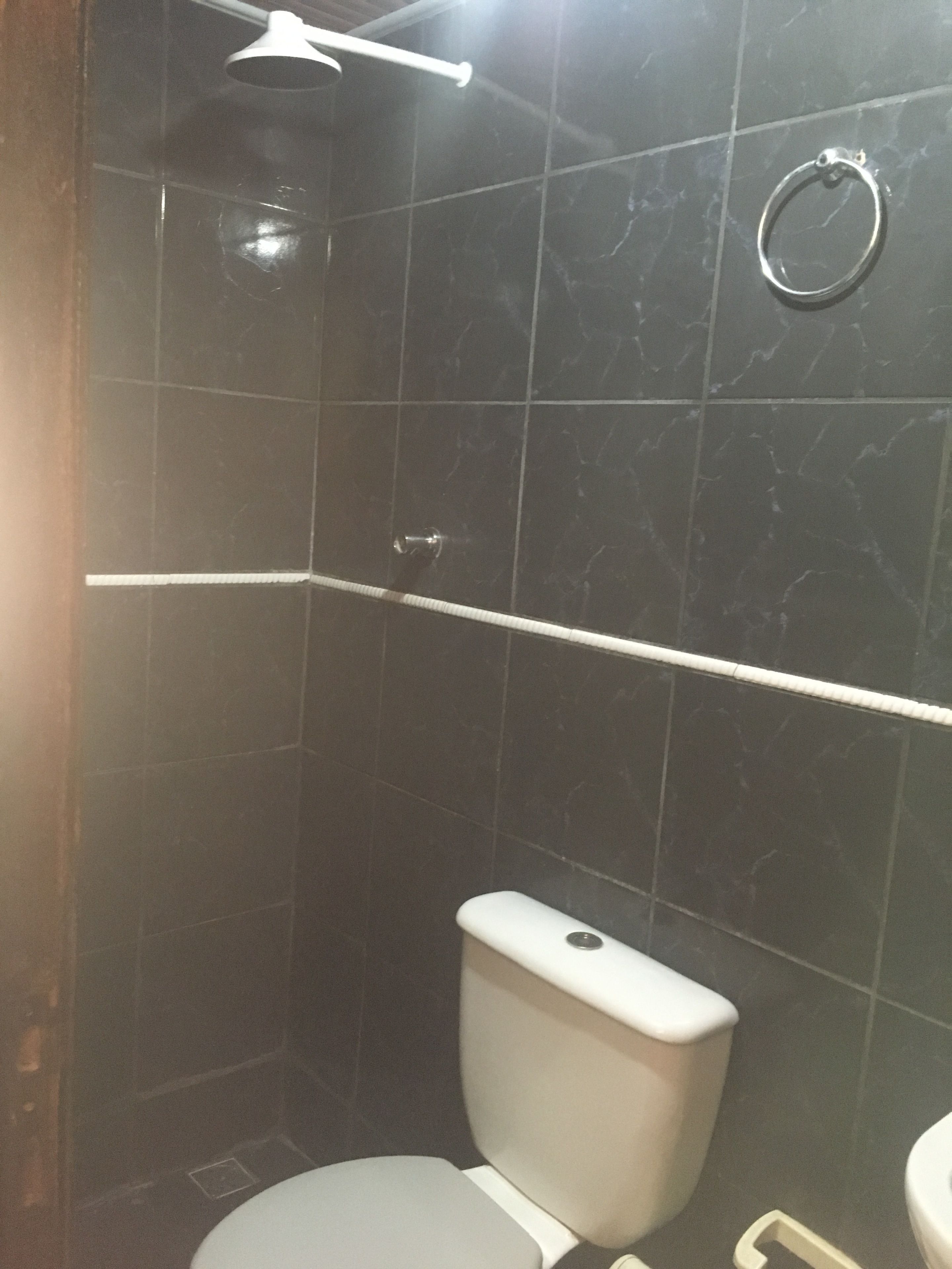 Un bagno con pareti rivestite di piastrelle scure, un WC bianco e uno spazio doccia.