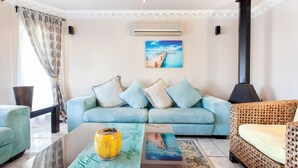 A living room with a light blue sofa, a wicker armchair, and a coffee table with a yellow vase. - Villa West Beach (Cape Town)