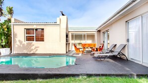 A residential backyard with a swimming pool, a patio with lounge chairs, and a dining area. - Villa West Beach (Cape Town)
