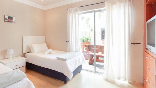 A bedroom with a bed, a nightstand, a TV, and a sliding glass door leading to an outdoor area. - Villa West Beach (Cape Town)