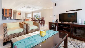A spacious living room with wicker furniture, a glass coffee table, and a flat-screen TV. - Villa West Beach (Cape Town)