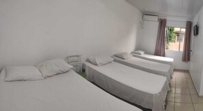 Una habitación con tres camas individuales, una mesita y una ventana con cortinas.