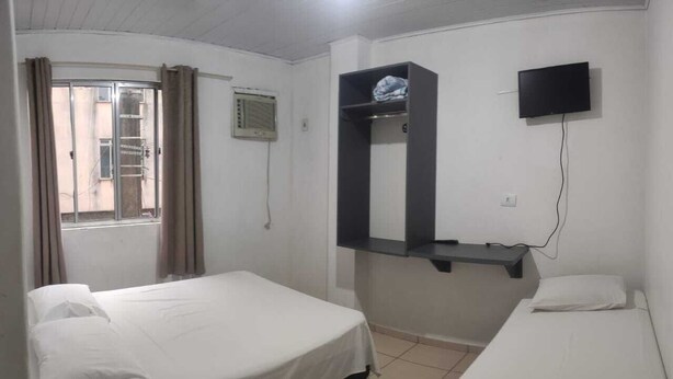 Una habitación con dos camas, un televisor montado en la pared y una ventana con cortinas.