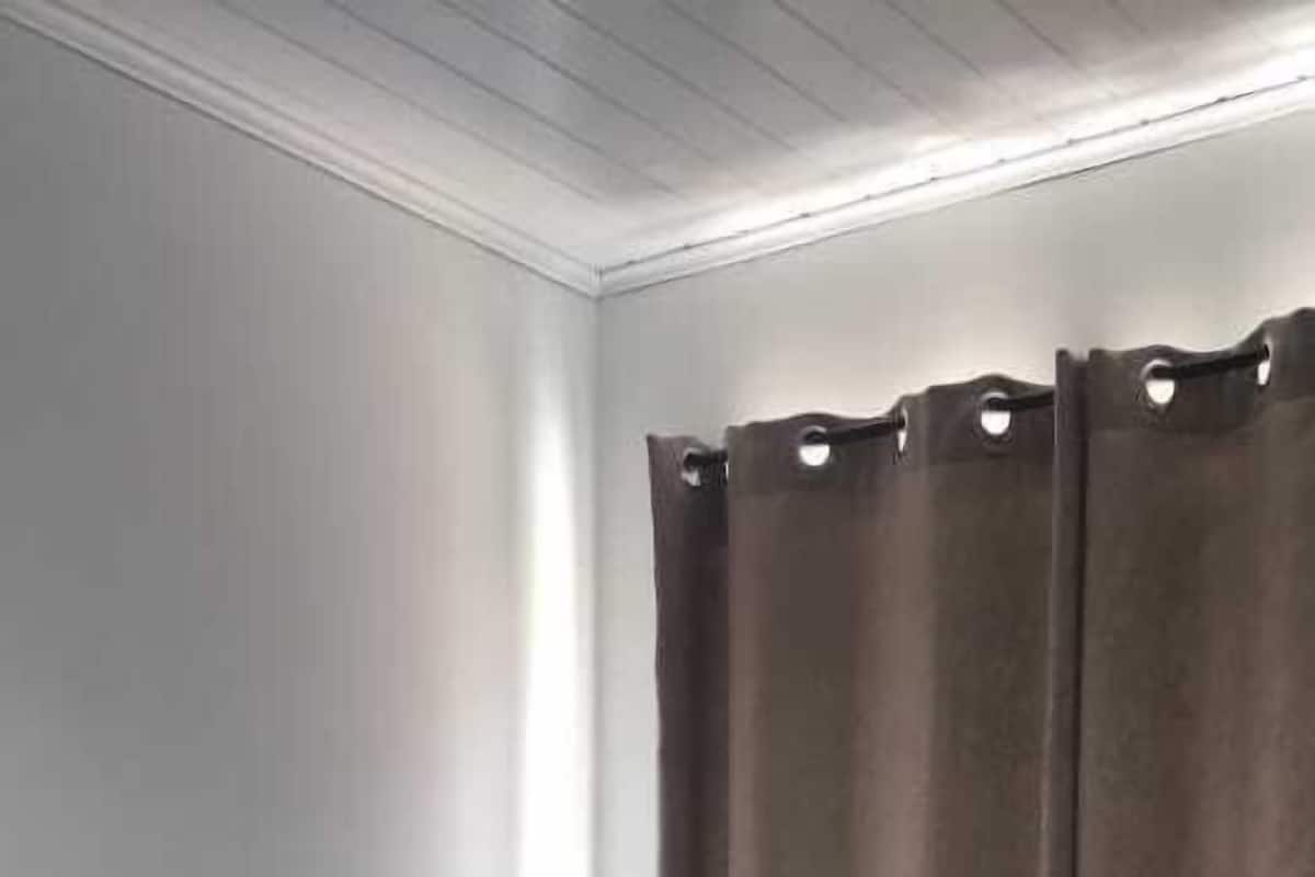 En säng för en person med vita sängkläder i ett rum med vita väggar och ett fönster med bruna gardiner.