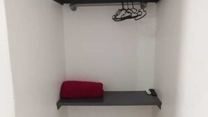 Una esquina de una habitación con dos estanterías negras, una con un cojín rojo y la otra con un objeto negro.