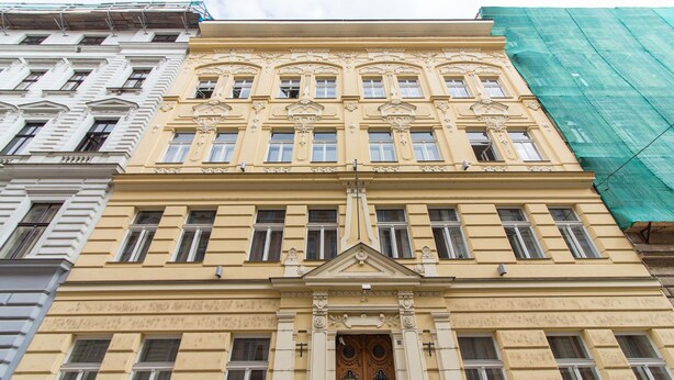 A multi-story building with a classical architectural style, featuring ornate window frames and decorative elements around the entrance.