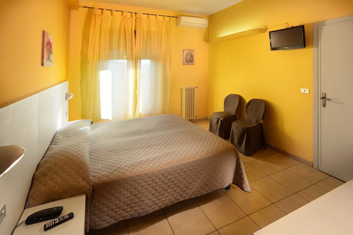 A hotel room with a bed, two chairs, a TV, and a door.