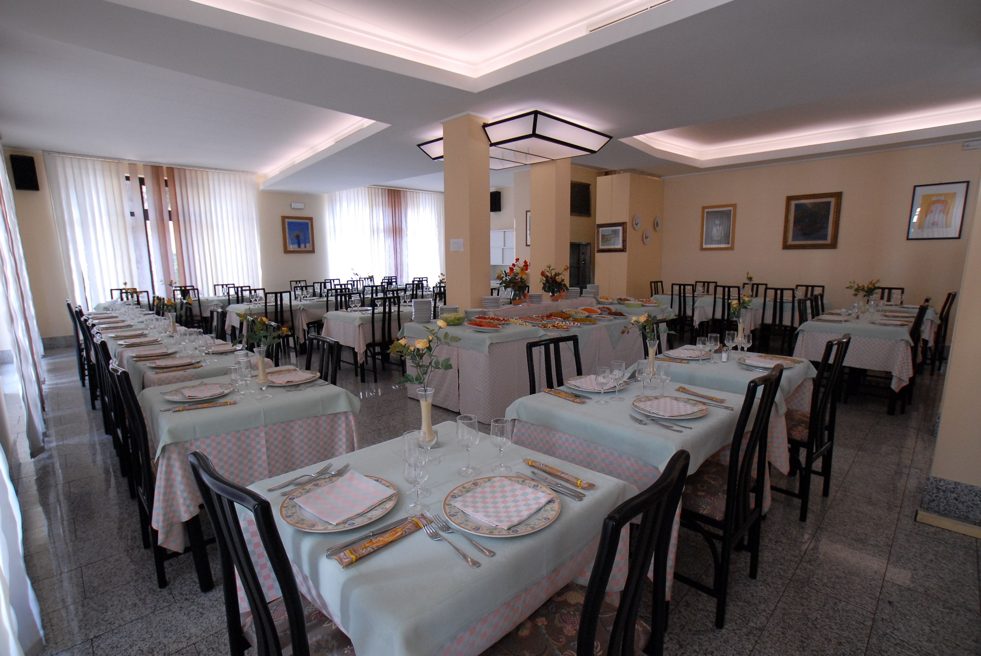 Un'ampia sala da pranzo con numerosi tavoli apparecchiati, impreziosita da un'elegante composizione floreale al centro e opere d'arte alle pareti.