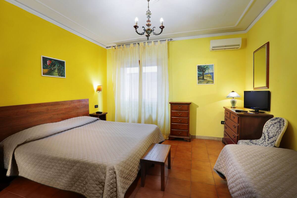 A hotel room with a bed, a chair, a dresser, a television, and a window with curtains.