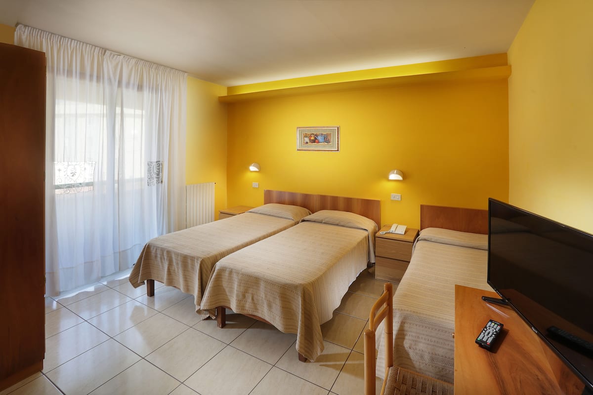 A hotel room with two beds, a television, a remote control, and a window with curtains.