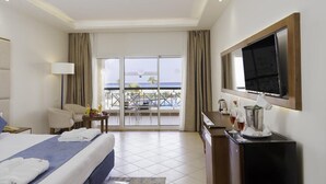 A hotel room with a bed, a desk, a TV, and a balcony with a view of the ocean. - Cyrene Island Hotel (sharm el sheikh)