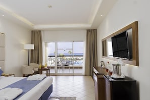 Quarto de hotel com cama, escrivaninha, televisão e varanda com vista para o oceano.