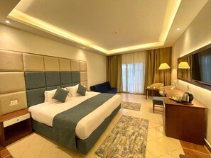 A hotel room with a large bed, a desk, a chair, a television, and a window with curtains. - Cyrene Island Hotel (sharm el sheikh)