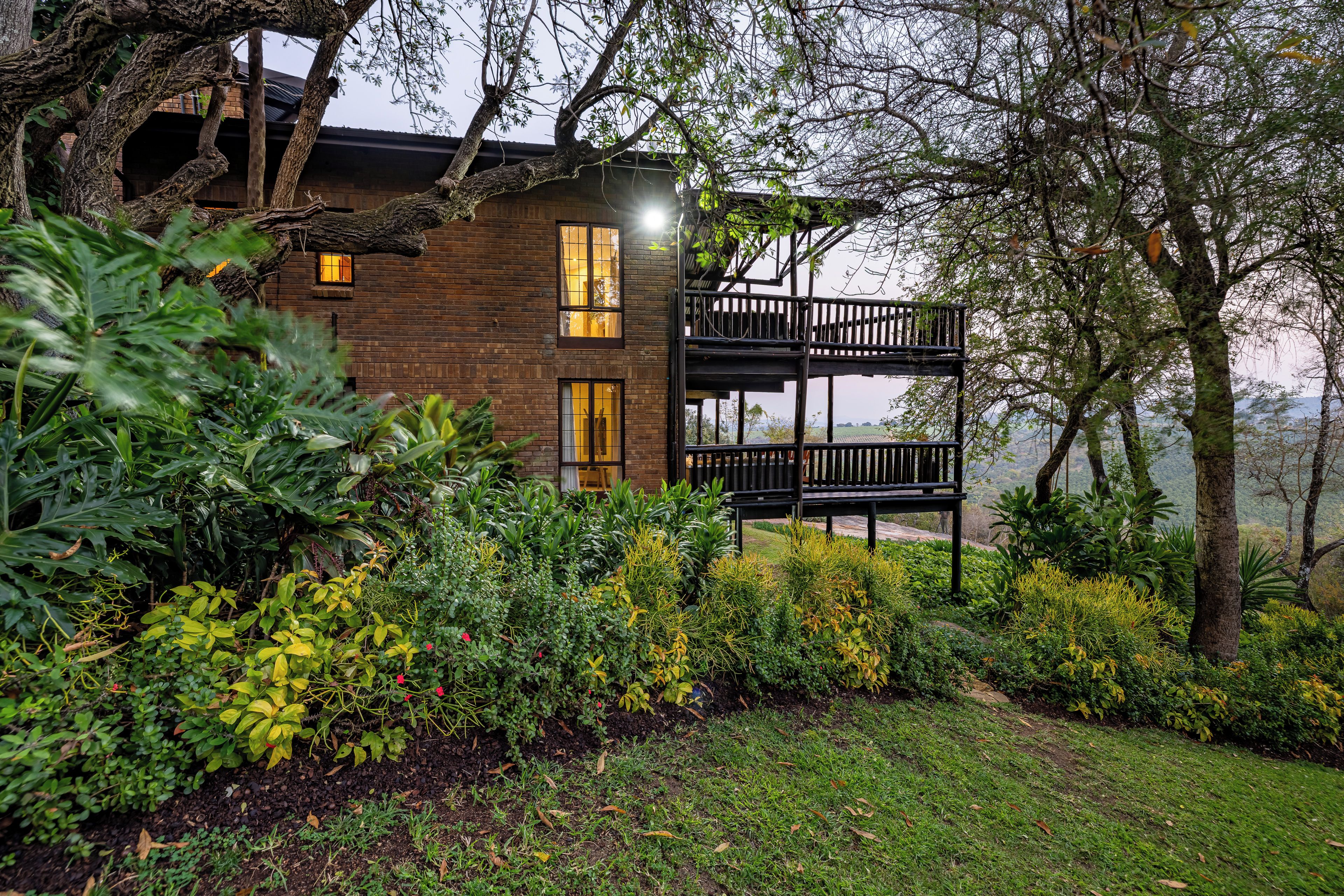 A two-story building with a balcony, surrounded by lush greenery and a view of the landscape.