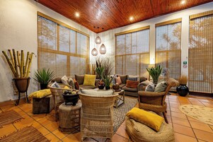 Un salón acogedor con mobiliario de mimbre, techo de madera y ventanas grandes con persianas de bambú.
