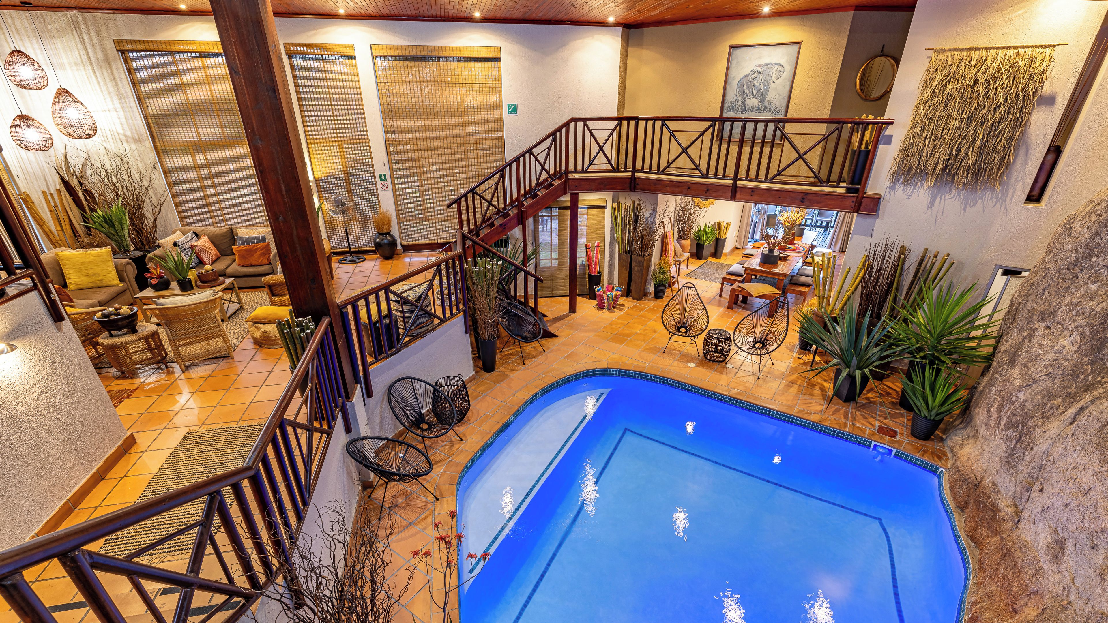 A spacious indoor area with a pool, wooden staircase, and various seating arrangements.