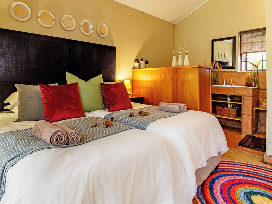A hotel room with a large bed, multiple pillows, a nightstand with a lamp, a wooden cabinet, and a colorful rug.