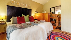 A hotel room with a large bed, multiple pillows, a nightstand with a lamp, a wooden cabinet, and a colorful rug. - Ulwazi Rock Lodge (Mbombela)