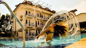 Una piscina con una persona sumergida, una escalera metálica y un edificio con balcones al fondo.