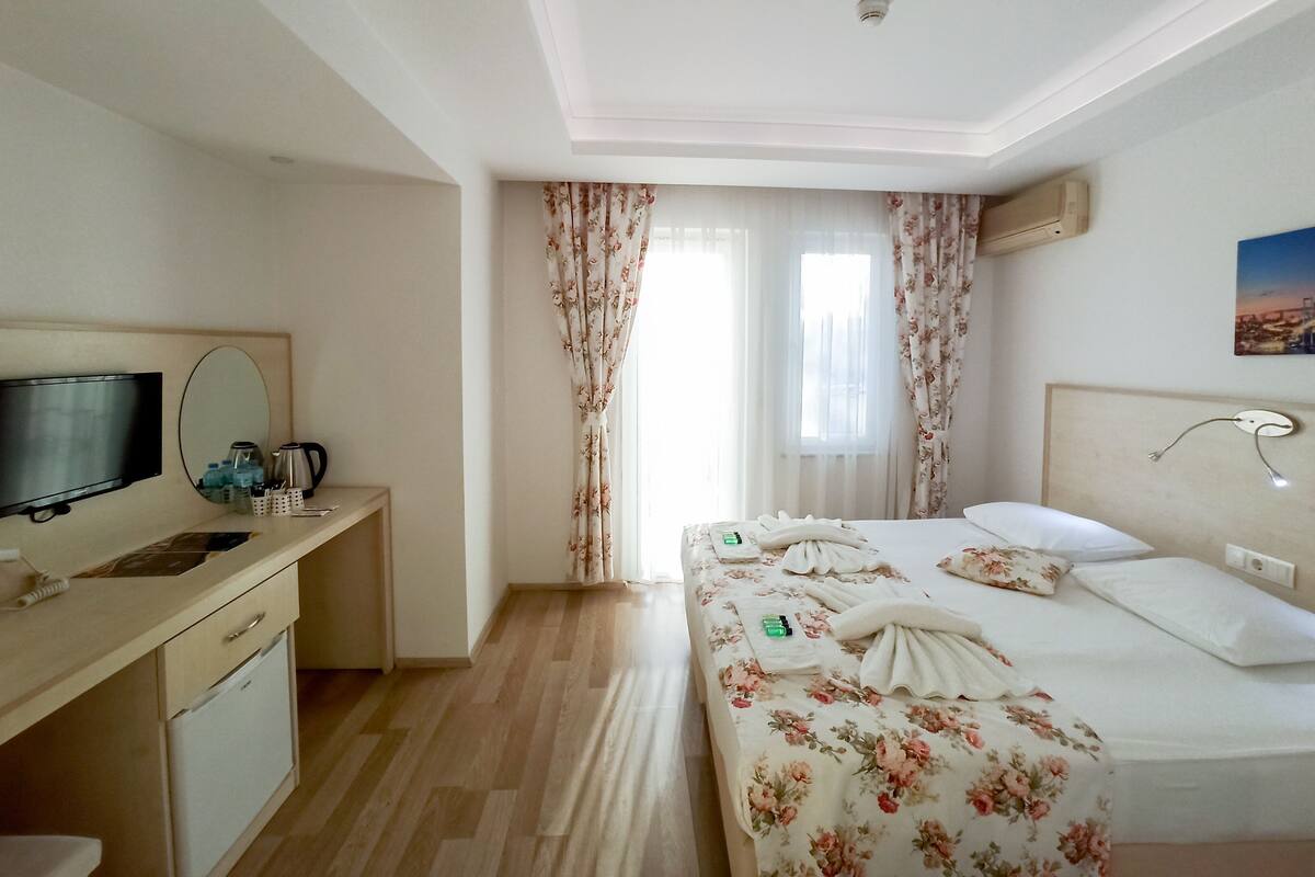 A hotel room with a bed, a desk with a television, a mirror, and a window with curtains.