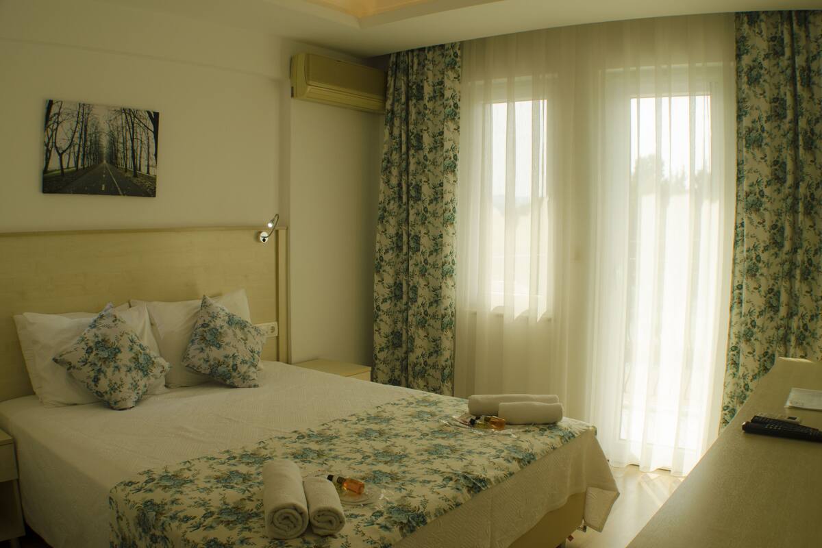 A hotel room with a bed, pillows, a bedside table with a remote control, and a painting on the wall.